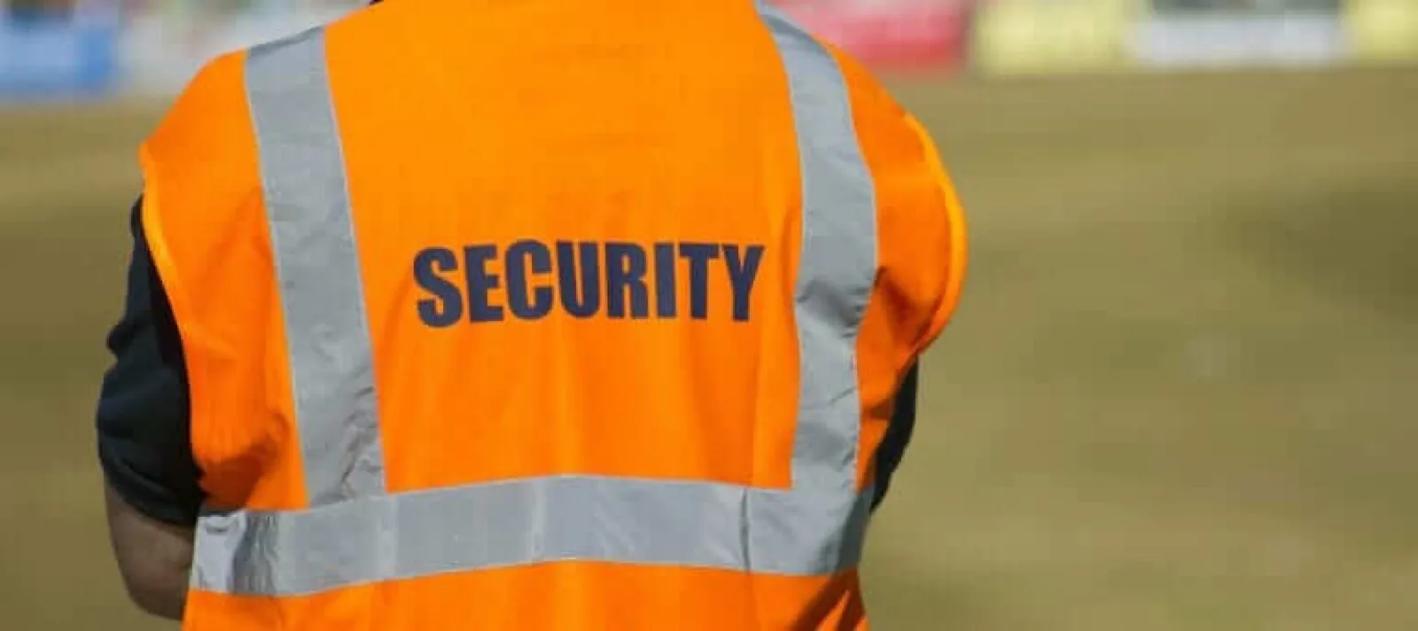 Security officer viewed from behind in an orange hi-vis SECURITY tabard while on duty at a UK outdoor event