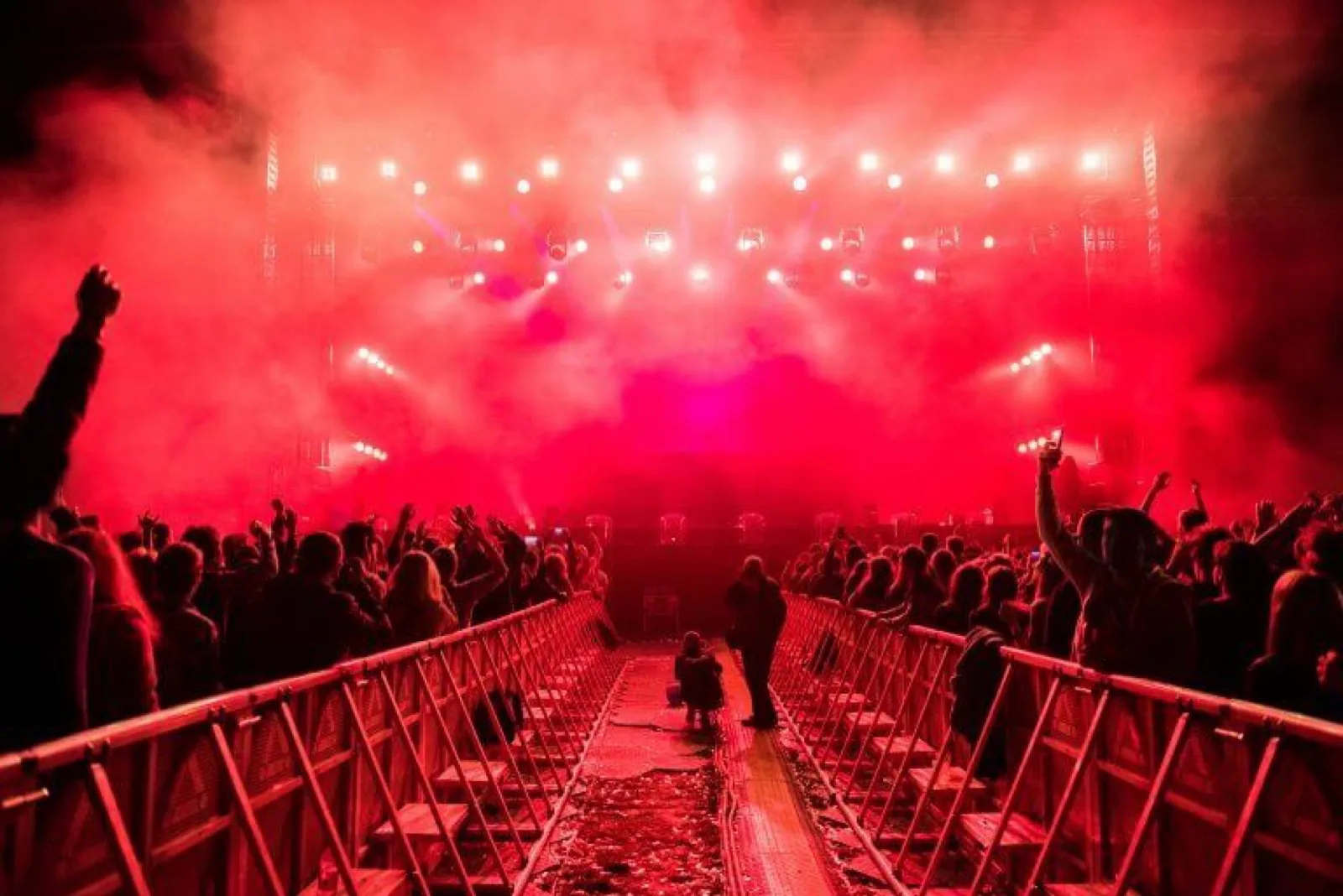 Event crowd lit in red in front of a concert stage, where walkie talkie teams coordinate stewarding, security and production