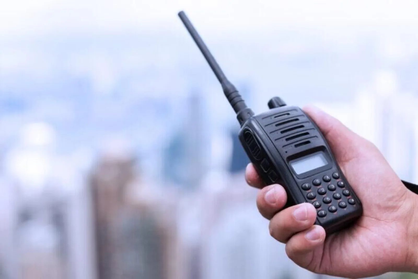 Professional black two-way radio held up against a city skyline, used for instant business communication between teams