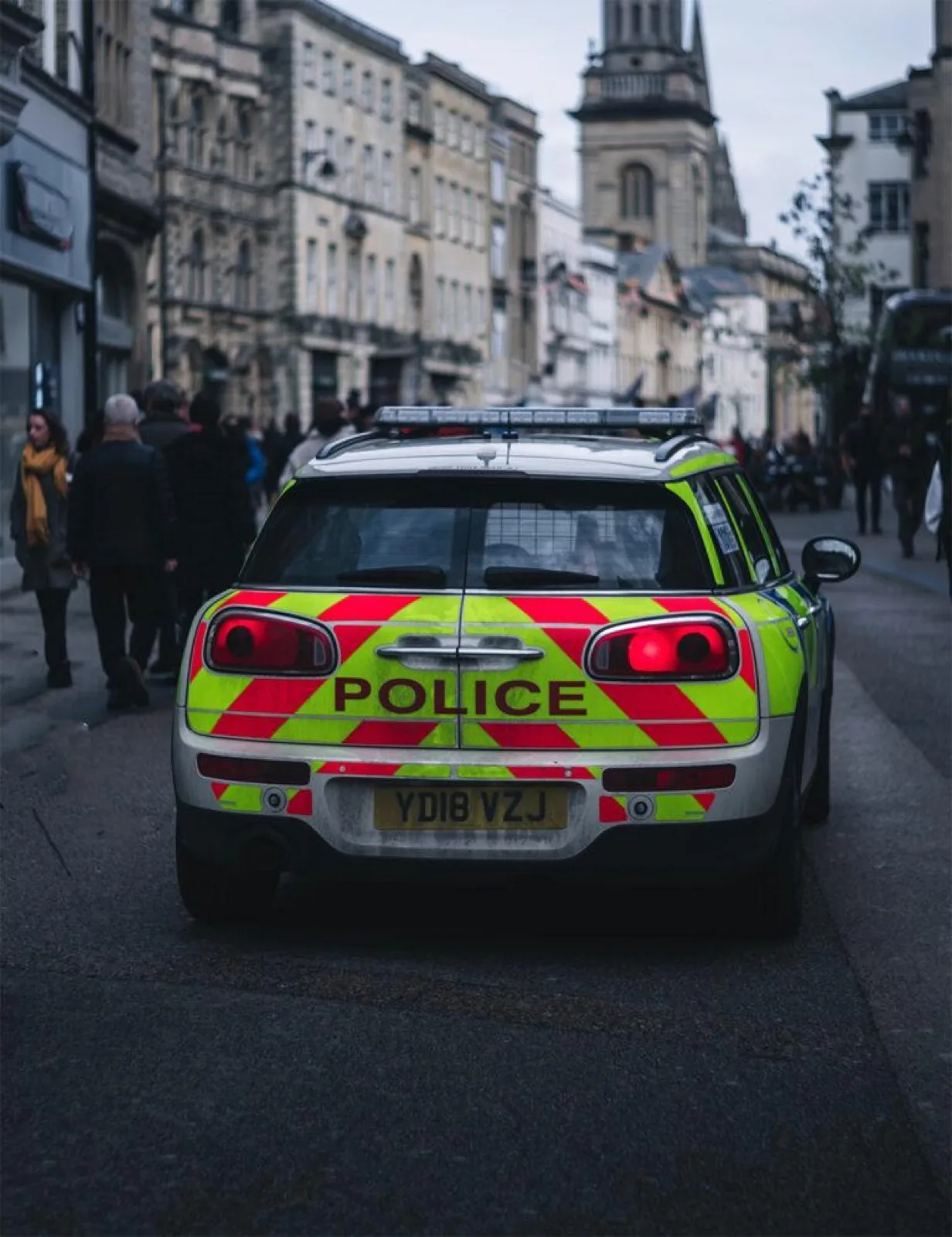 Marked UK police response car in Battenburg livery on a British high street, crew coordinated by police two-way radio