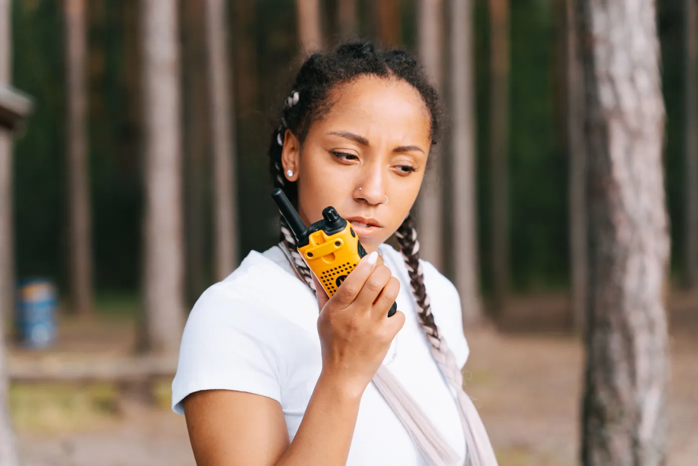 Woman holding a yellow handheld two-way radio while working outdoors at an event.