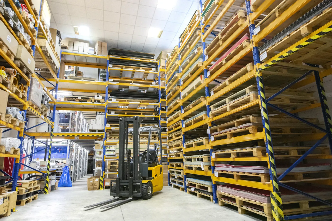Forklift in a warehouse aisle between tall pallet racking loaded with stock