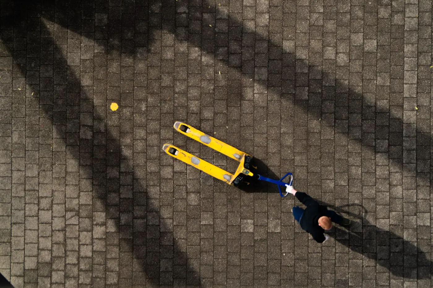 Aerial view of a lone worker pulling a pallet truck in an open yard, out of sight of colleagues.
