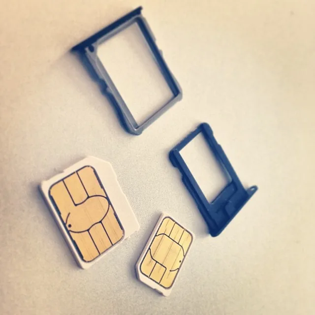 A micro SIM and a nano SIM beside their phone trays, showing the size difference