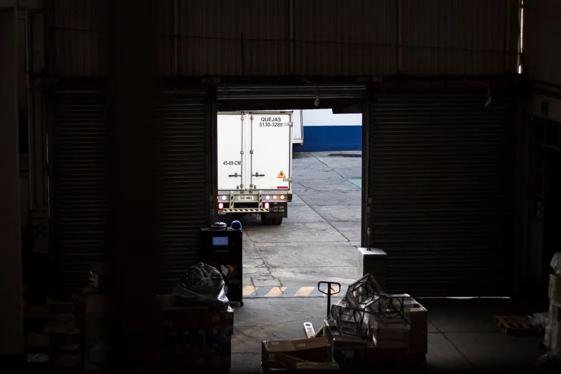 Delivery lorry at a warehouse loading bay, seen from inside the building as goods-in prepares to unload