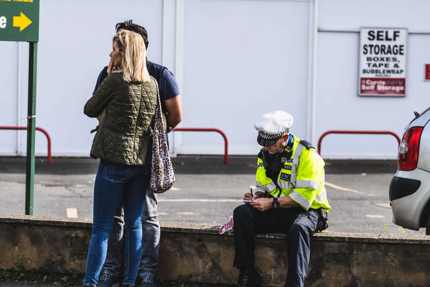 UK police officer in a hi-vis jacket taking a written statement from members of the public at a roadside incident